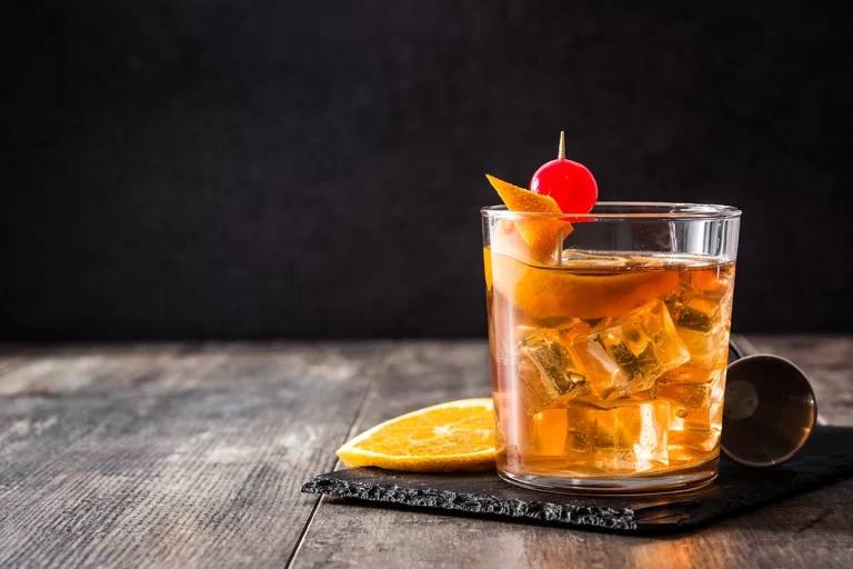 Brown Cocktail with Orange and Cherry Garnish